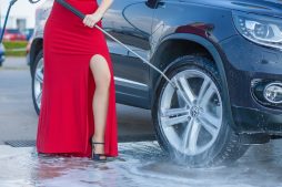 Frau mit rotem aufreizenden Kleid putzt Auto